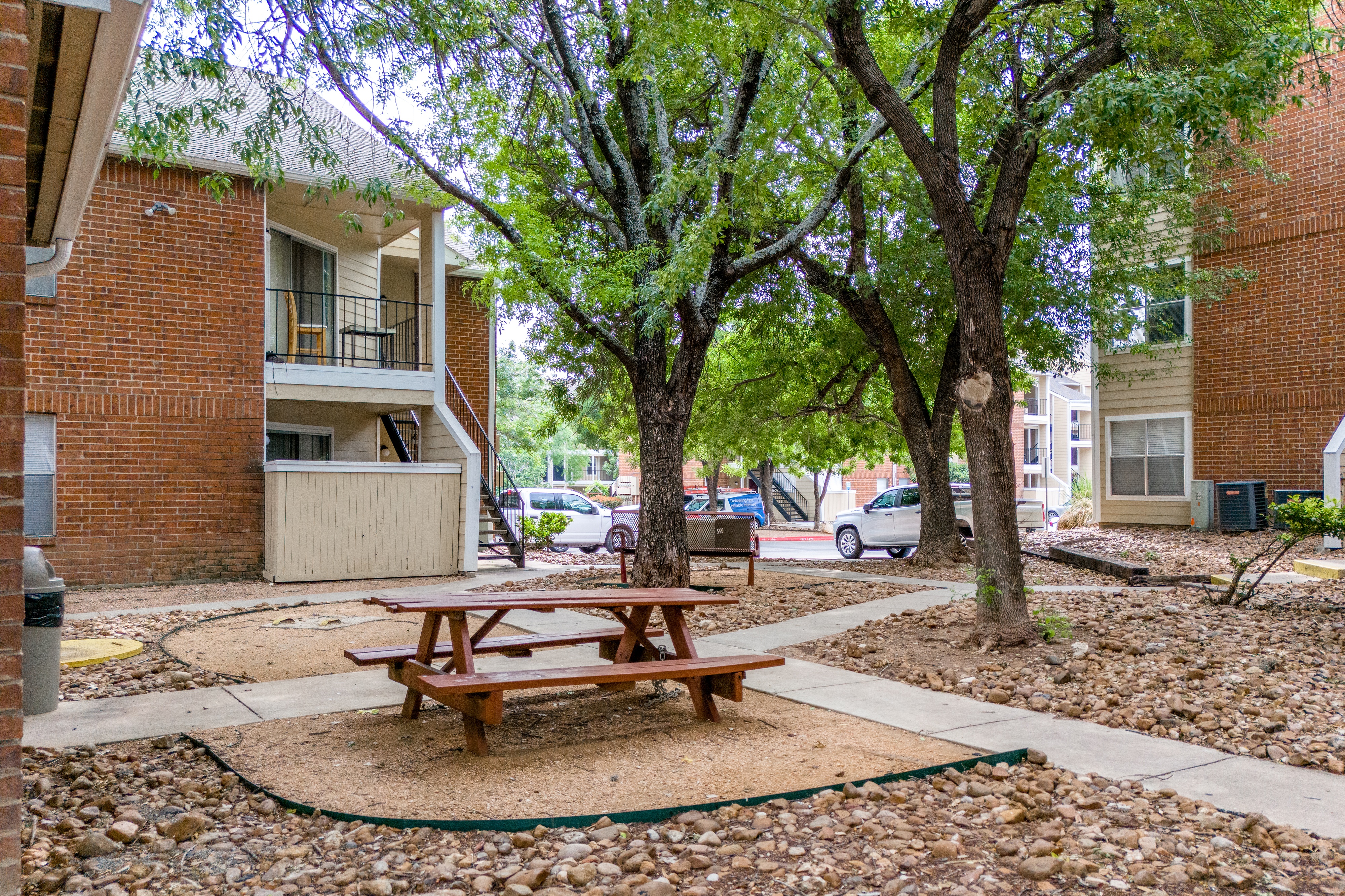 A picnic table sits in the middle of a gravel area between two apartment buildings.